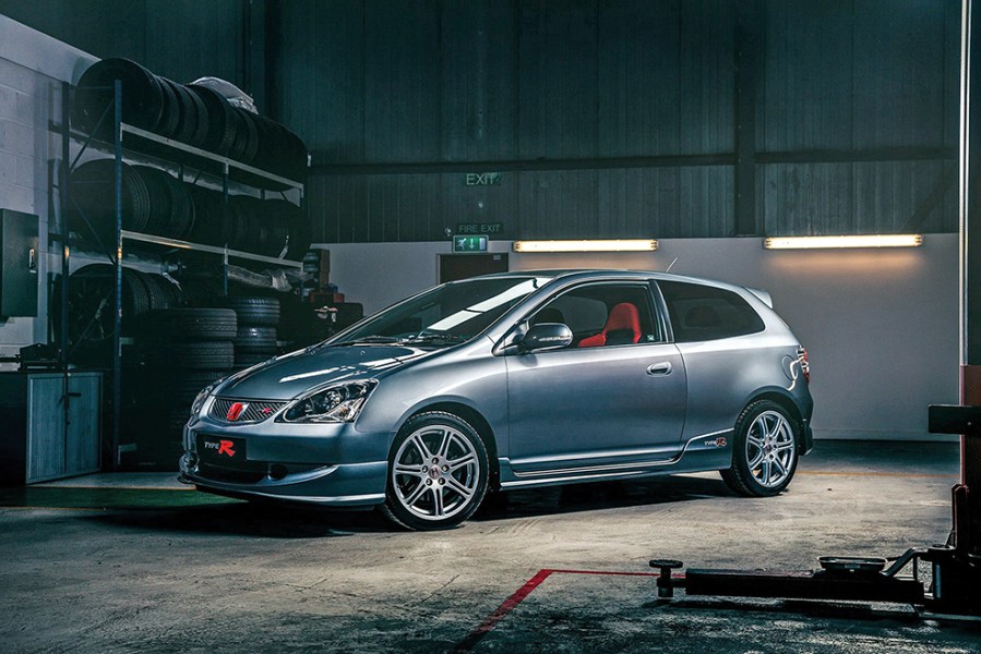 A front left shot of a dark grey 2005 Honda Civic Type R with red interior inside a garage