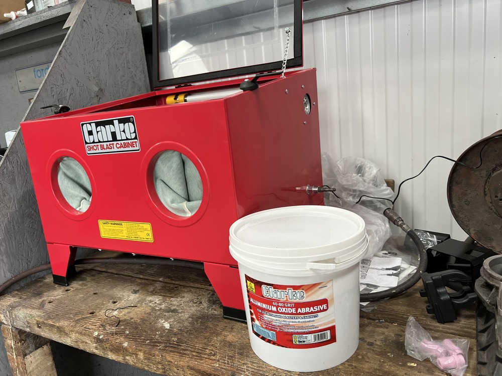 Clarke shot blasting cabinet with pot of blasting grit beside it.