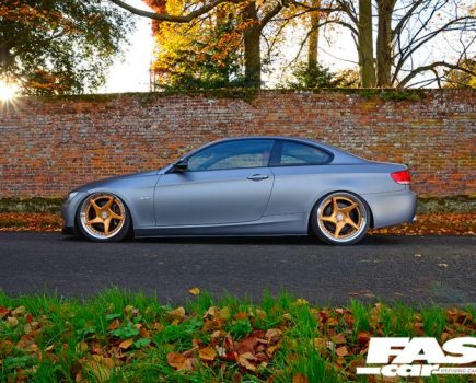 Matte silver BMW-335I-E92 with gold rims and a red brick backdrop